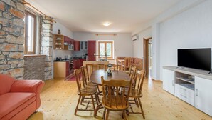 A spacious living room with a wooden dining table, red sofa, and a TV on a wooden cabinet.