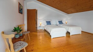 A bedroom with two beds, wooden flooring, a ceiling with exposed beams, a small table with a lamp, a chair, and a potted plant.