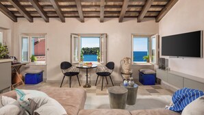 A living room with a wooden ceiling, a TV mounted on the wall, and a view of the sea through large windows. - Natasha's Beachfront (Rovinj)