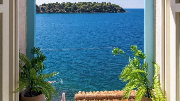 A window with a view of a calm sea and a distant island. - Natasha's Beachfront (Rovinj)