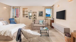 A modern bedroom with a bed, a sofa, a chair, a TV, and a view of the sea. - Natasha's Beachfront (Rovinj)