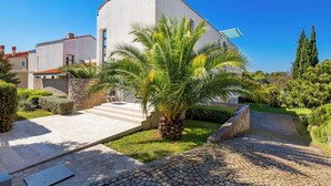 A modern building with a white facade, a paved entrance, and a small palm tree in the foreground. - RM Grande Villa (Rovinj)