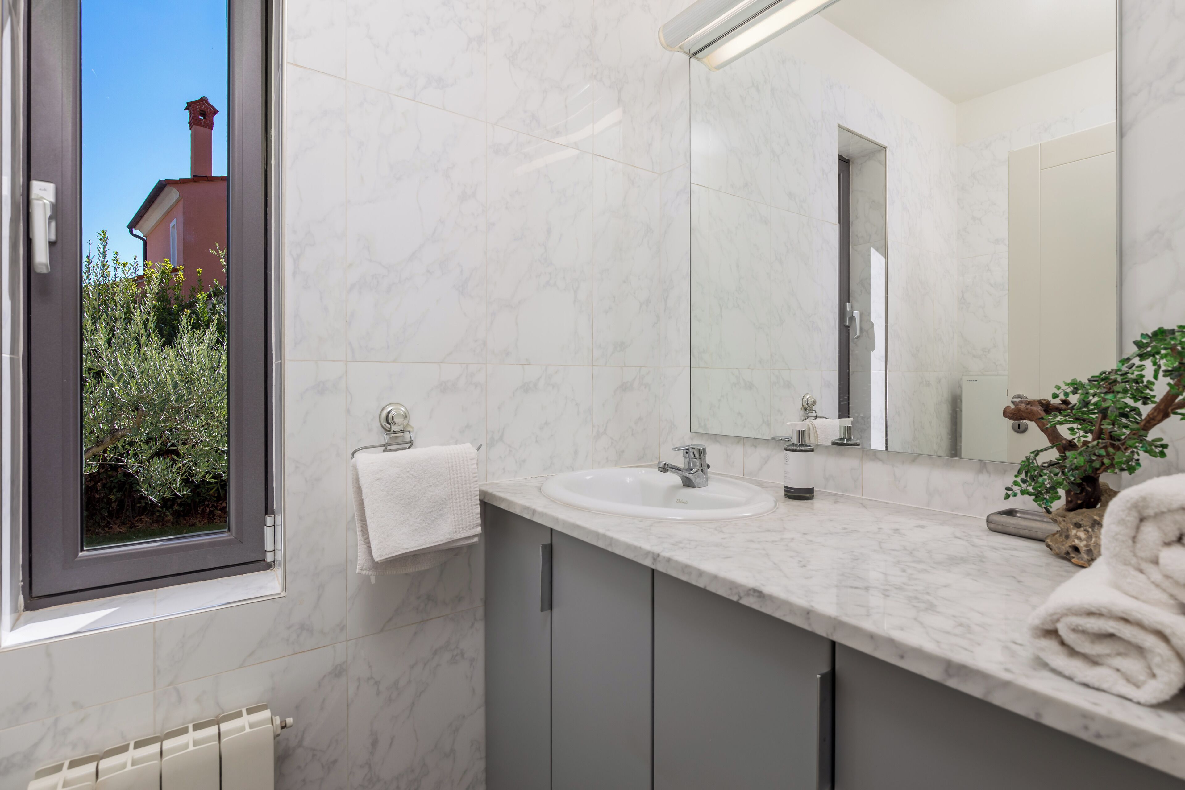 A bathroom with a large window, a sink, a mirror, and a towel rack.
