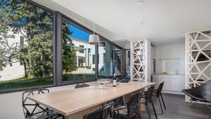 A modern dining area with a long table, multiple chairs, and a view of the outdoors through large windows. - RM Grande Villa (Rovinj)