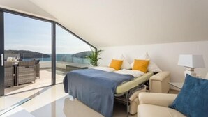 A modern bedroom with a bed, a sofa, and a glass door leading to a balcony. - Luxury Apartment Anto (Medulin)