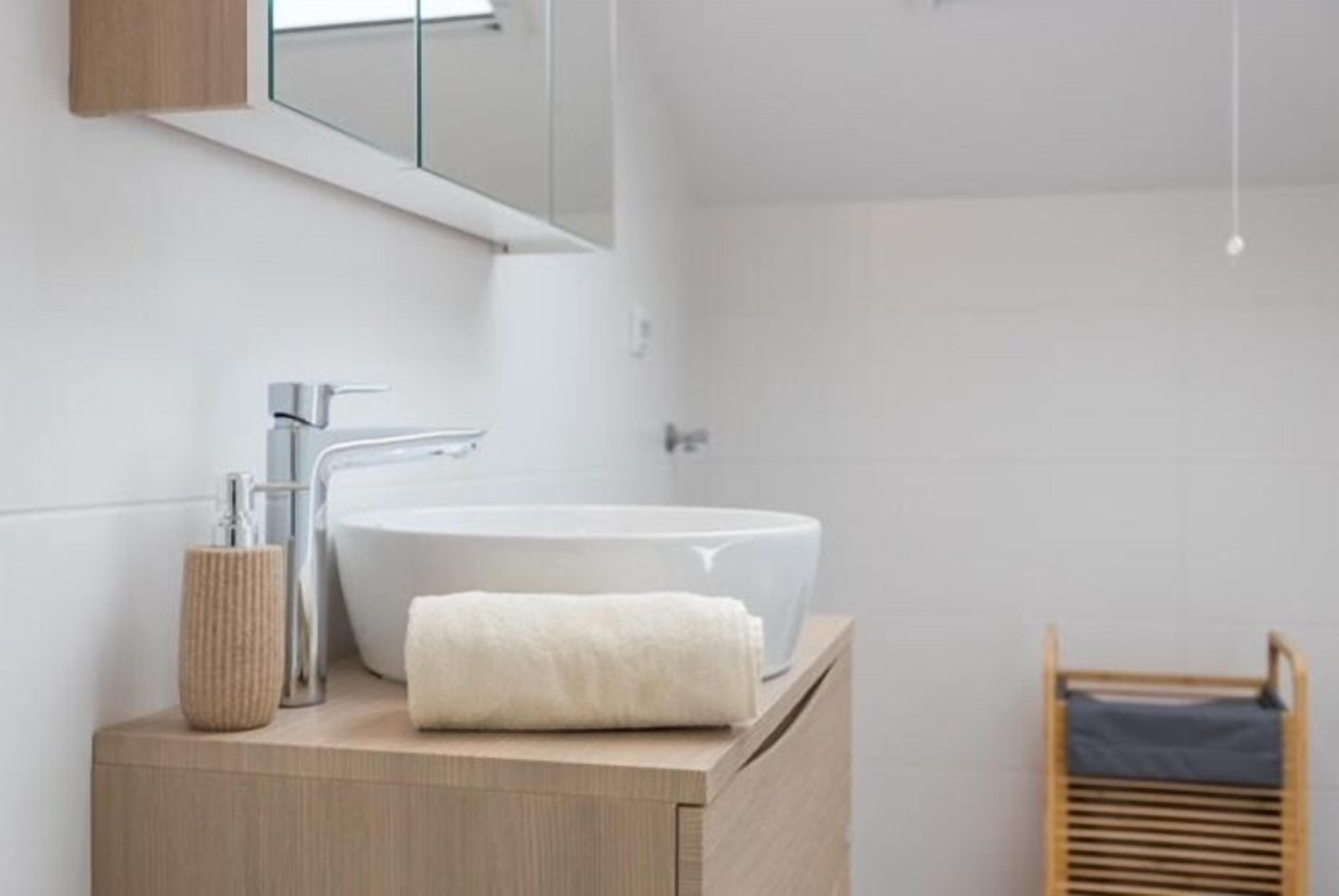 A modern bathroom with a large white sink, a wooden vanity, a mirror, and a towel.