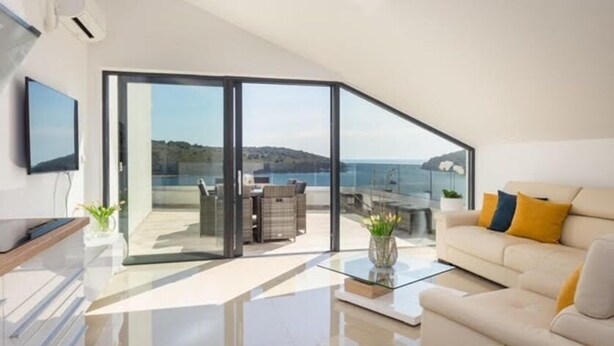 A modern living room with a glass sliding door leading to a balcony with a view of the sea. - Luxury Apartment Anto (Medulin)