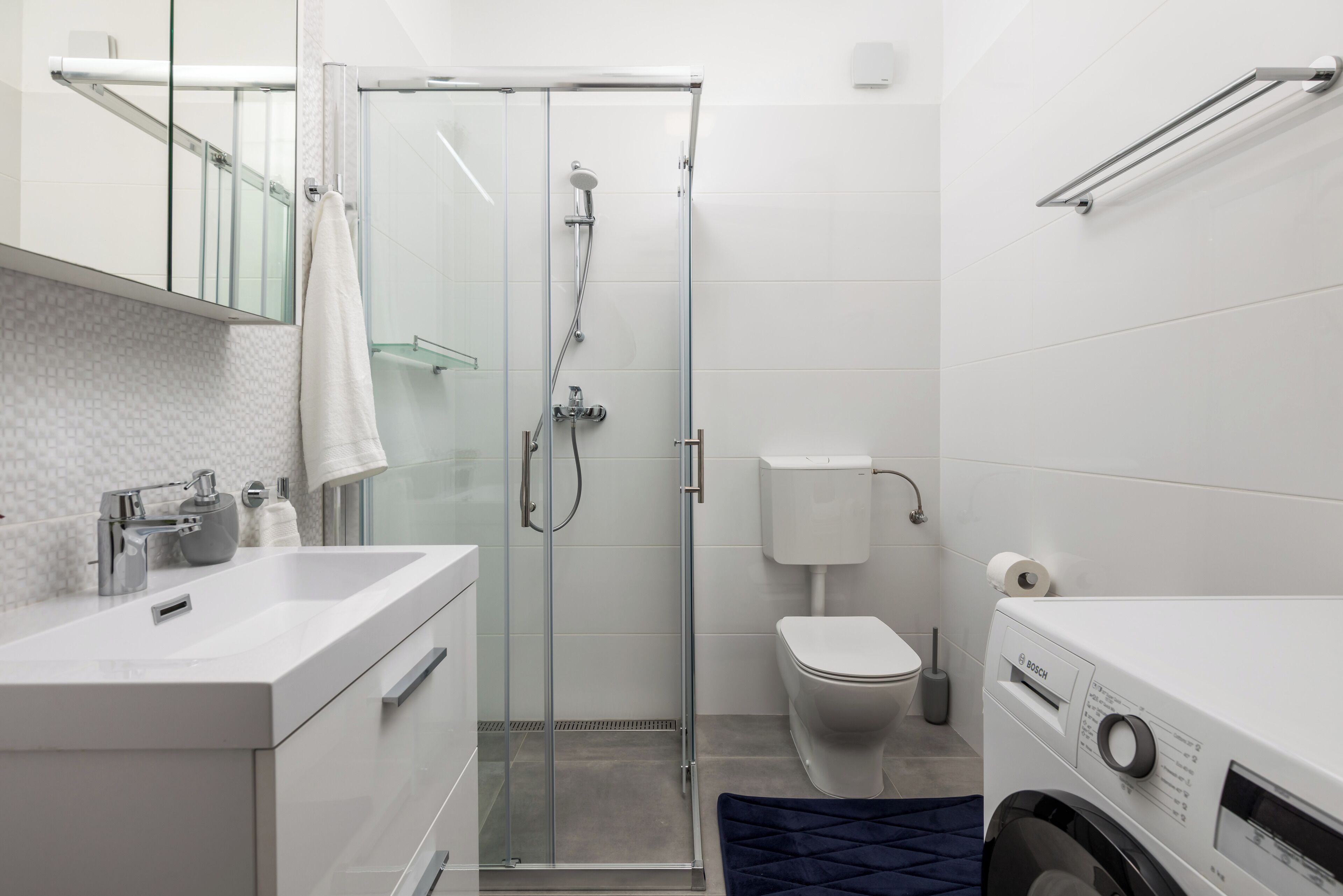 Un bagno moderno con doccia vetrata, un water bianco e una lavatrice Bosch.