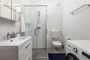 Un baño moderno con ducha cubierta con vidrio, inodoro blanco y lavadora Bosch.