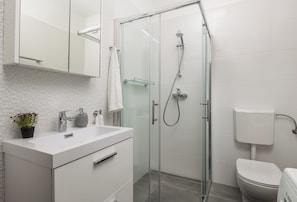 A modern bathroom with a glass-enclosed shower, a white sink, and a toilet. - Apartment Isola (Rovinj)