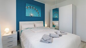 Un dormitorio moderno con una cama grande, una mesita de noche con lámpara, un aparador y un espejo montado en la pared.