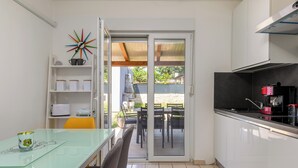 Una cocina moderna con armarios blancos, una mesa de comedor de vidrio y una puerta corrediza de vidrio que da a un patio exterior.