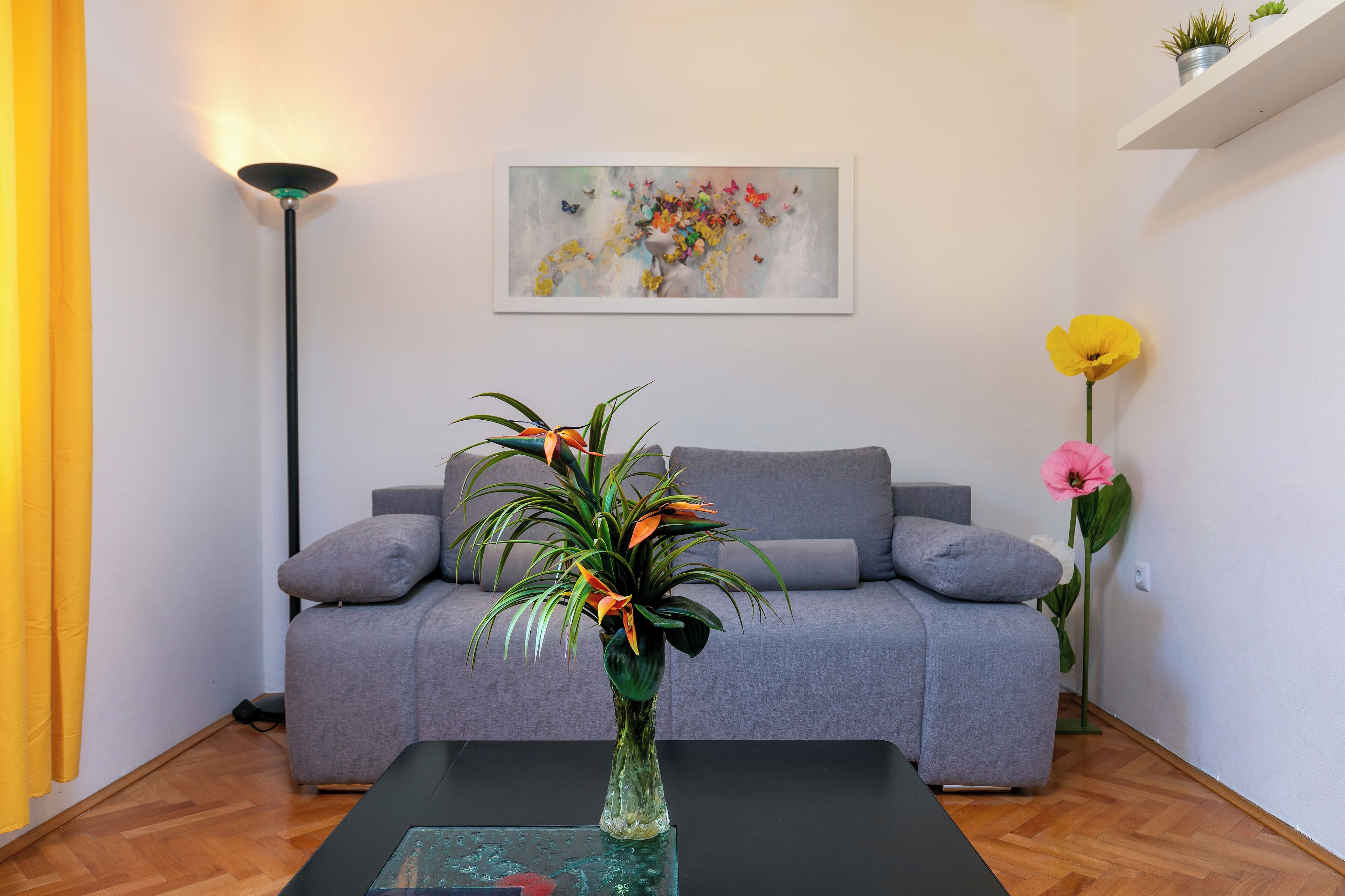 Un salon avec un canapé gris, une table basse noire et un vase rempli de fleurs.