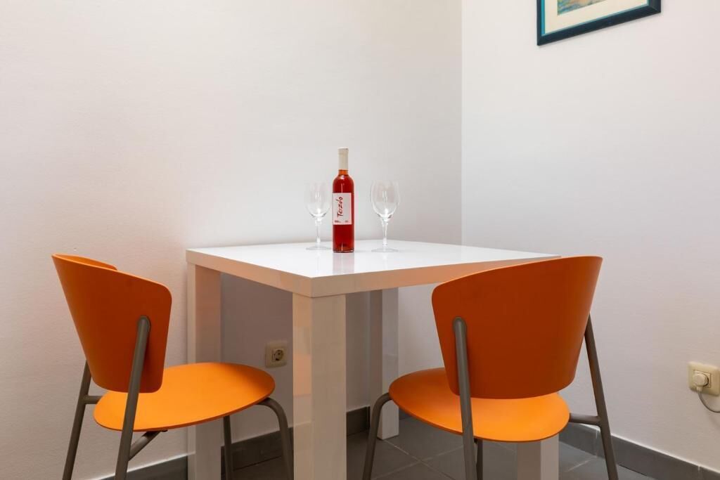 Een eettafel met twee oranje stoelen, een fles rode wijn en twee wijnglazen.