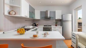 Una cucina moderna con mobili bianchi, una cappa aspirante in acciaio inossidabile, un frigorifero e un'area pranzo con tavolo e sedie.