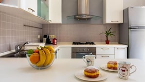 Una cucina moderna con mobili bianchi, un piano cottura a gas e un lavandino. Sul bancone c'è una ciotola di frutta e due pasticcini.