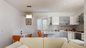 Un ambiente compatto con divano, tavolo da pranzo, sedie e angolo cottura.
