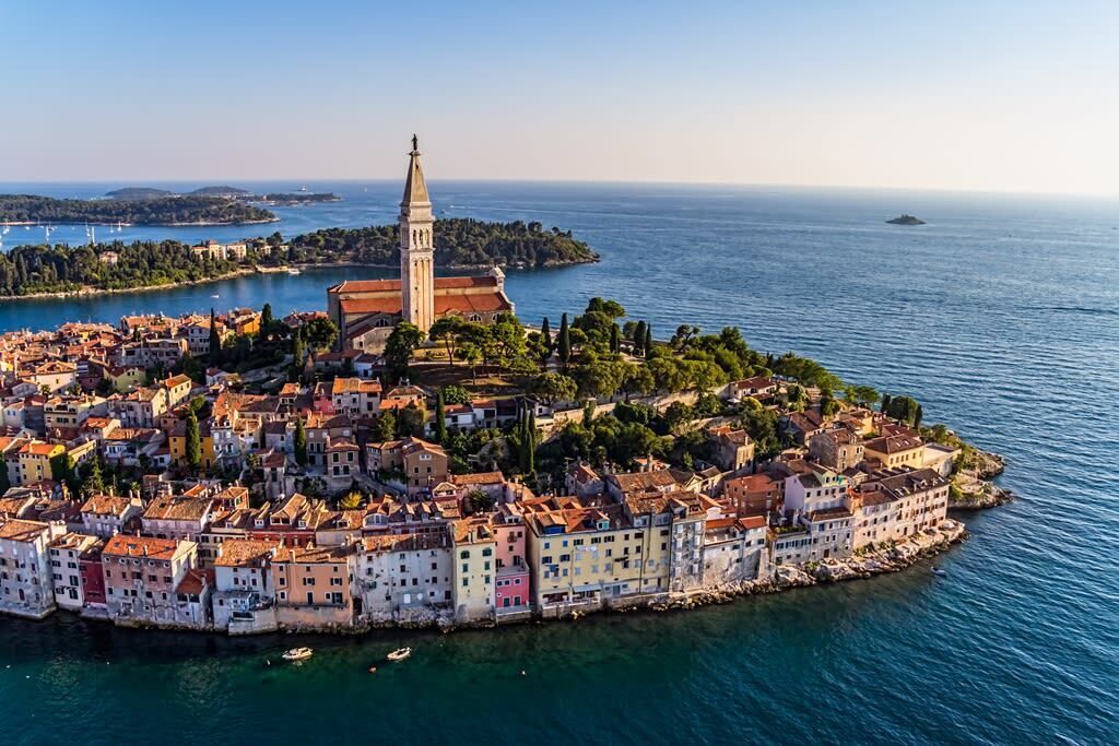 Eine Küstenstadt mit einem markanten Kirchturm, umgeben von bunten Häusern und freiem Blick auf das Meer.