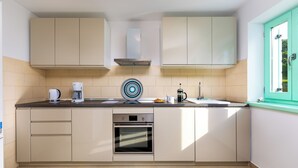 Eine moderne Küche mit beigen Schränken, einem Edelstahlbackofen, einer Kaffeemaschine und einem Fenster mit grünem Rahmen.