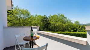 Ein Balkon mit rundem Tisch, zwei Stühlen, einer Weinflasche und einem Glas auf dem Tisch.