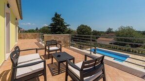 Un balcón con mobiliario exterior, una piscina y vistas del paisaje circundante.