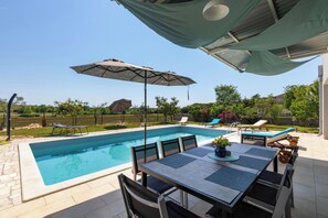 A rectangular swimming pool with a tiled deck, surrounded by lounge chairs and a table with chairs. - Villa Cvek (Kanfanar)