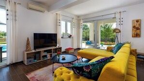Una sala de estar moderna con un sofá amarillo, un televisor de pantalla plana y un comedor con una mesa y sillas.