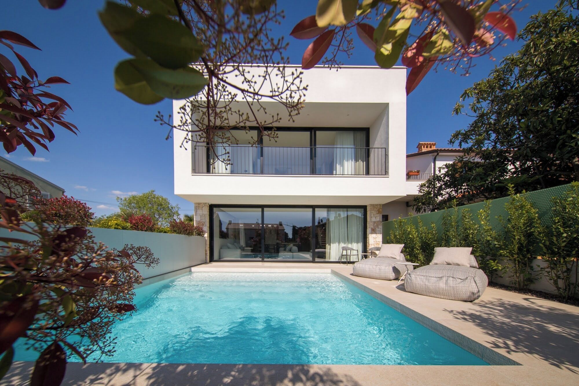 A modern two-story house with a swimming pool, large windows, and outdoor seating.