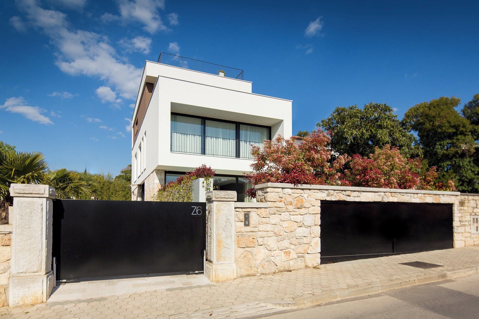 A modern two-story house with a stone wall and a black gate.