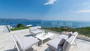 A modern outdoor seating area with a glass balustrade overlooking a coastal landscape. - Villa Atrium (Labin)