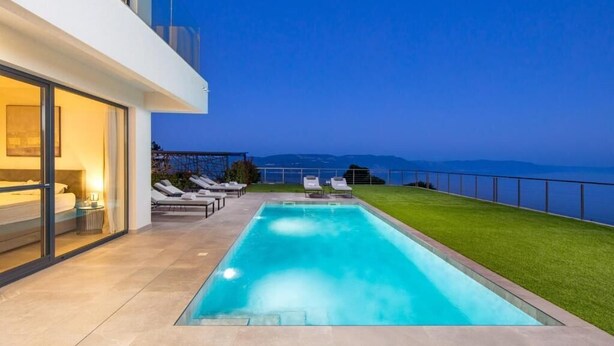 A modern pool area with a clear view of the sea, a grassy lawn, and a balcony with lounge chairs. - Villa Atrium (Labin)