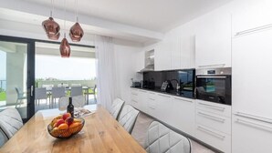 A modern kitchen with white cabinets, a wooden dining table, and a fruit bowl. - Villa Atrium (Labin)