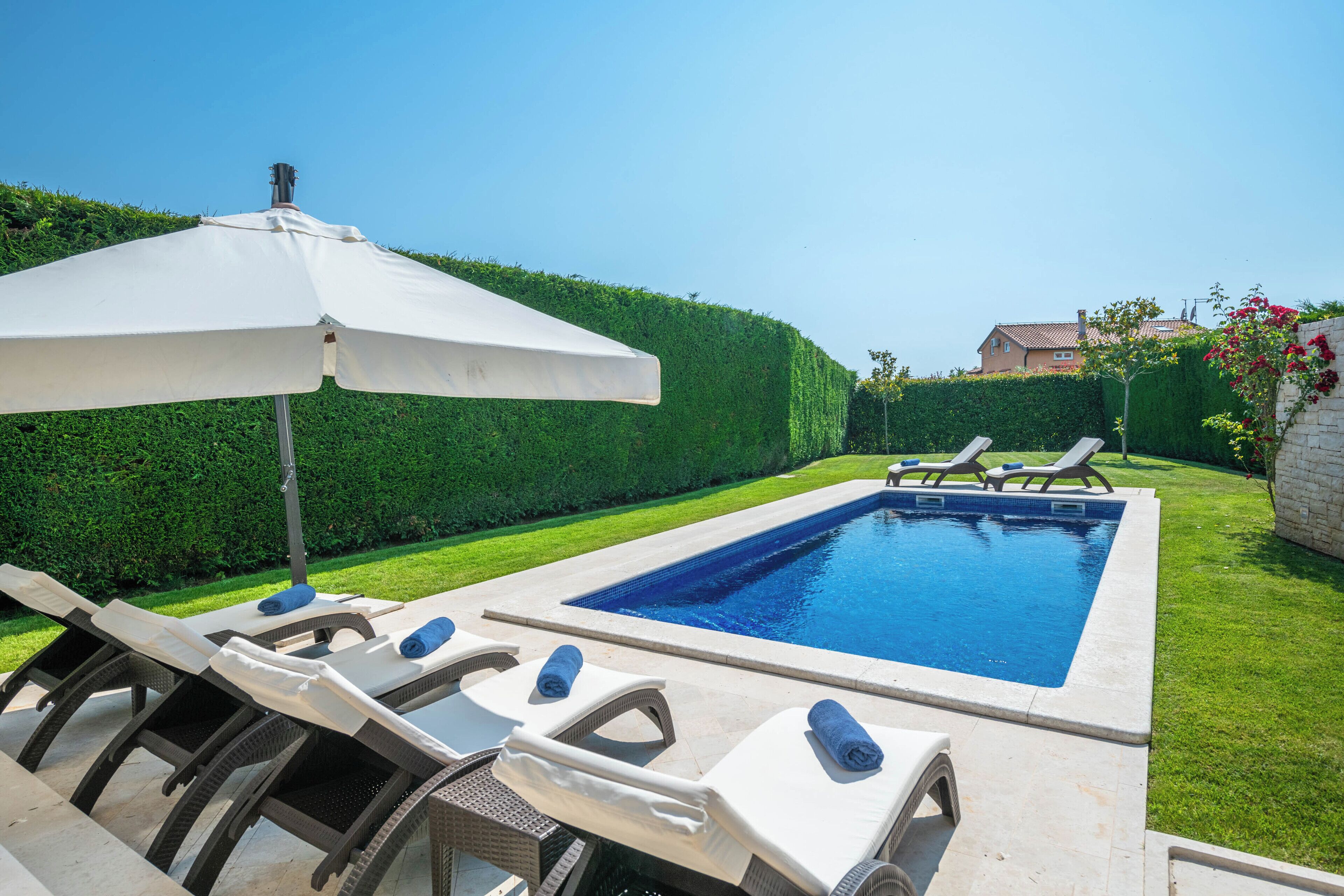 A rectangular swimming pool with lounge chairs and a white umbrella.