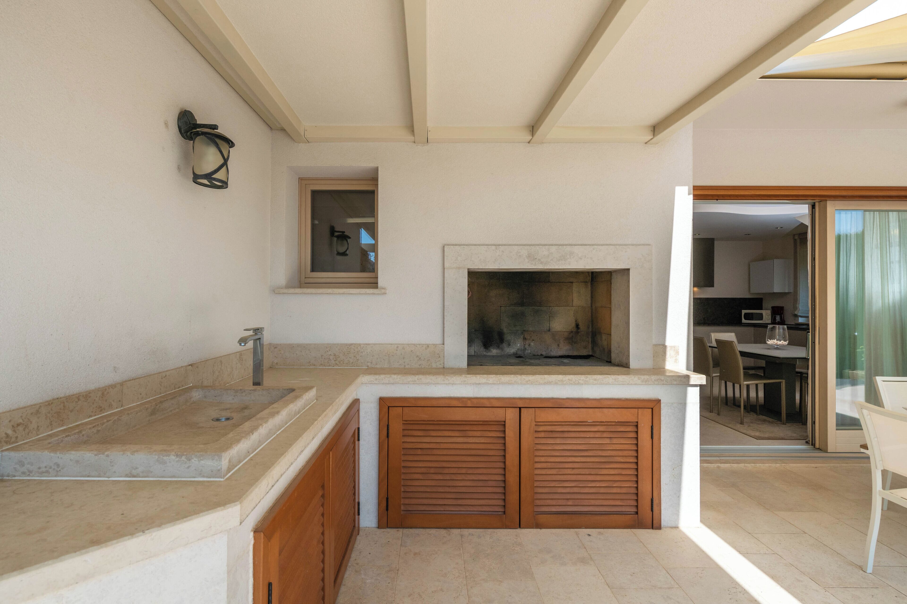 Una cocina con pileta integrada, muebles de madera, chimenea y un comedor visible a través de una puerta abierta.