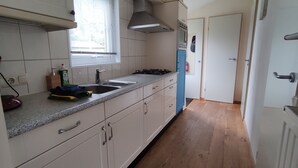A kitchen with white cabinets, a granite countertop, a stove, and a window with blinds. - Boshuisje Wageningen (Wageningen)