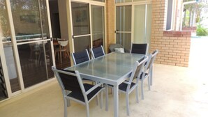 A glass-top table with six chairs, a brick wall, and a sliding glass door leading to an indoor area. - Annette's - by Lifestyle. Brunswick Heads (BRUNSWICK HEADS)