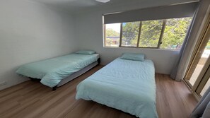 A room with two single beds, a window with a view of trees, and a sliding door.