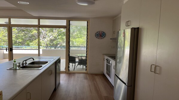 A modern kitchen with a stainless steel refrigerator, a sink with a faucet, and a window overlooking a balcony.