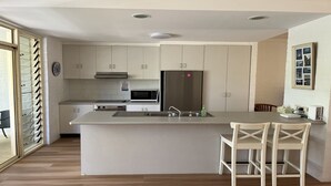A modern kitchen with white cabinets, stainless steel appliances, and a central island with bar stools. - Annette's - by Lifestyle. Brunswick Heads (BRUNSWICK HEADS)