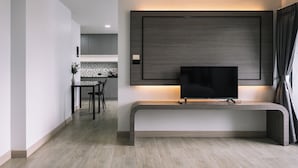 A modern living room with a flat-screen TV mounted on a wall, a built-in bench, and a kitchen area in the background. - Aston Residence hatyai (Hat Yai)