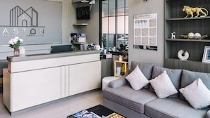 A modern reception area with a grey sofa, a coffee table, and a reception desk. - Aston Residence hatyai (Hat Yai)