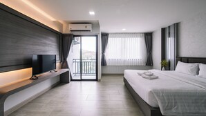 A modern hotel room with a flat-screen TV on a built-in shelf, a large bed with white linens, a balcony with a view, and an air conditioning unit on the wall. - Aston Residence hatyai (Hat Yai)
