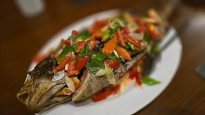 Un poisson entier, à la peau croustillante, garni de légumes coupés en dés et présenté sur une assiette blanche.