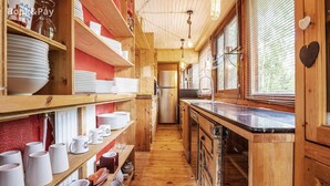 A wooden interior with shelves of white plates and mugs, a kitchen area with a refrigerator, and a window with blinds. - Rustic Mountain Chalet with Jacuzzi (Formiguères)