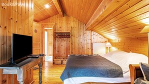 A wooden cabin room with a bed, a TV, and a lamp. - Rustic Mountain Chalet with Jacuzzi (Formiguères)