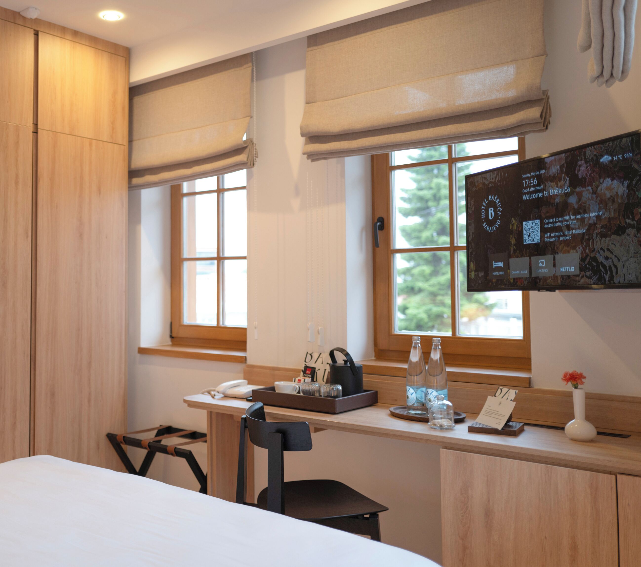 Ein Hotelzimmer mit Holzschreibtisch, Stuhl, Bett und Fenster mit Blick auf Bäume.