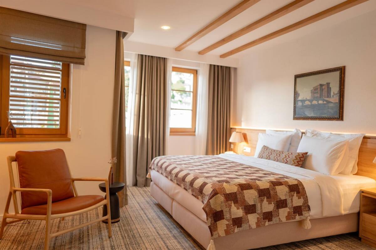 A bedroom with a bed, a chair, a nightstand, a lamp, and a painting on the wall.