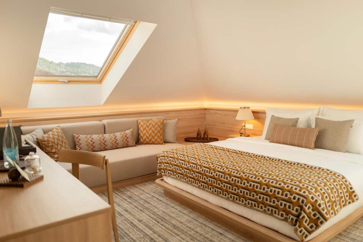 A bedroom with a skylight, a bed with patterned bedding, a bedside table, and a sofa.