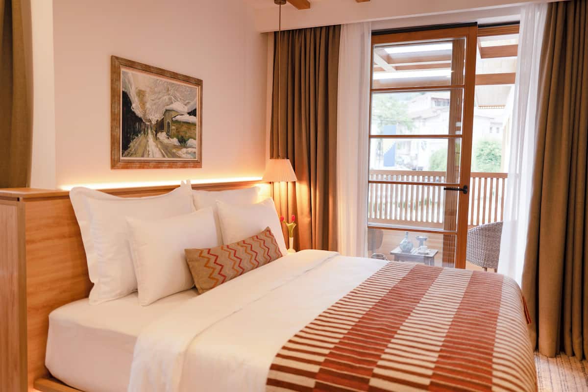 A hotel room with a large bed, a painting on the wall, and a view of the outside balcony.