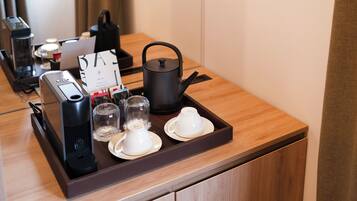 Habitación de hotel con una mesa de madera dispuesta para tomar té, una tetera, tazas y una máquina de café.